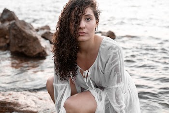 Woman Crouching On Rock Near Body Of Water
