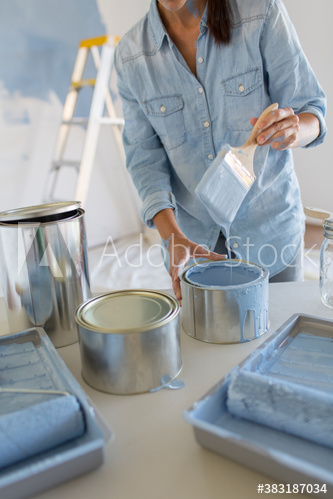 Woman dipping paintbrush into blue paint can