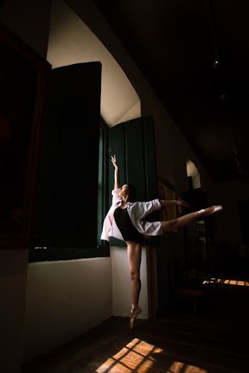 woman doing ballet pose in front of window during daytime