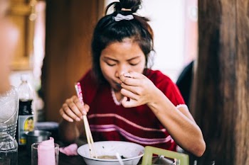 woman eating noodles while holding spoon and chopsticks