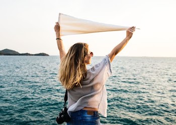 woman facing ocean while raising white pennant