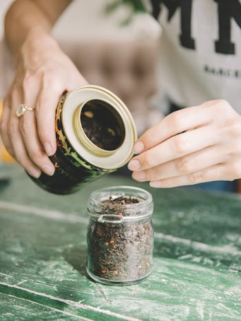 Woman filling glass container with tea leafs 