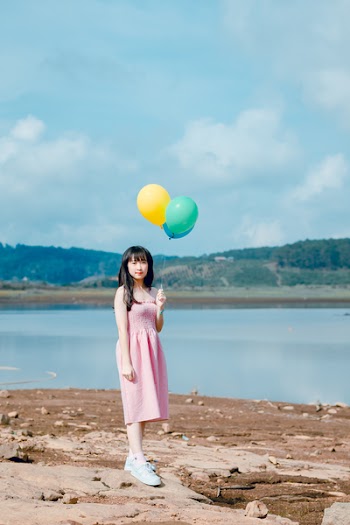 Woman Holding Balloons Standing on Beige Sand