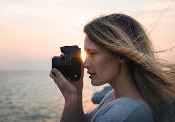 woman holding black bridge camera standing near beach