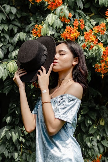 Woman Holding Black Hat Near Orange Flowers