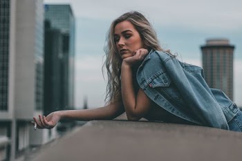 woman holding blue chambray jacket while smoking near buildings