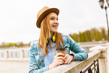 Woman Holding Brown Cup Leaning on Beige Concrete Hand Rails