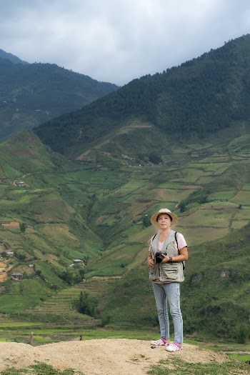 Woman Holding Camera In Front Of Green Mountain