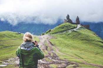 woman holding camera taking picture of castle on hill
