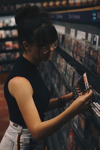 Woman Holding Cd Case Beside Cd Cases on Display Rack