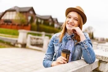 Woman Holding Cup of Tea Leaning on Fence