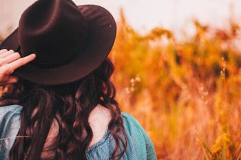 woman holding dress hat in front of brown plants