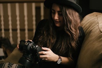 woman holding DSLR camera sitting on brown chair