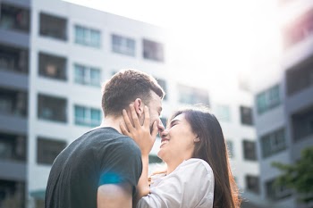 Woman Holding Face of Man Wearing Black Shirt Near White Building at Daytime