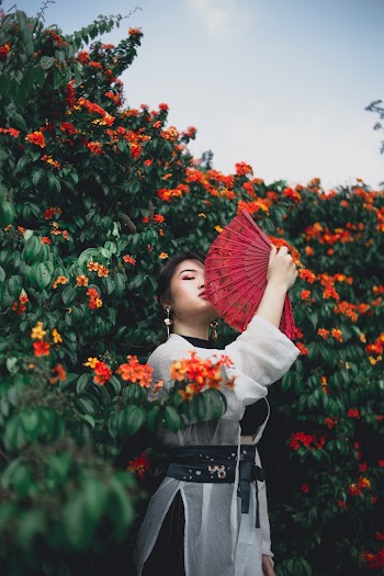 Woman Holding Fan Standing Near Bushes