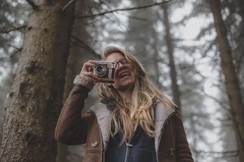 woman holding film camera in front of pine trees