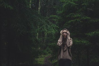 woman holding head standing between trees