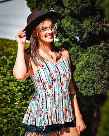 Woman Holding Her Brown Fedora Hat Standing in Front of Green Tress