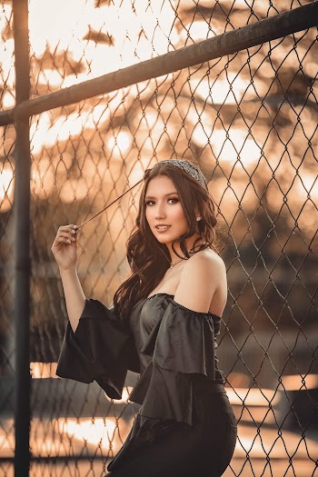 Woman Holding Her Hair While Leaning on Chain-link Fence