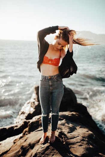 woman holding her hair while standing on rock formation beside body of water