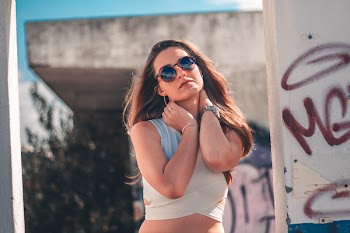 Woman Holding Her Neck Under Blue Skies Near White Wall