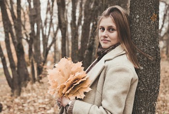 Woman Holding Leaves While Leaning Her Back on Tree