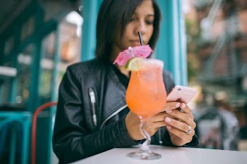 Woman Holding Mobile Phone with a Cocktail Glass on the Table