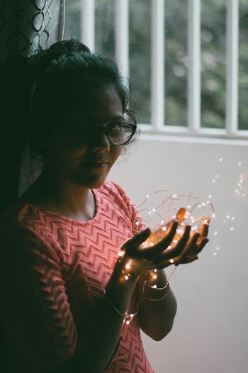 Woman Holding Orange String Lights Beside White Wall