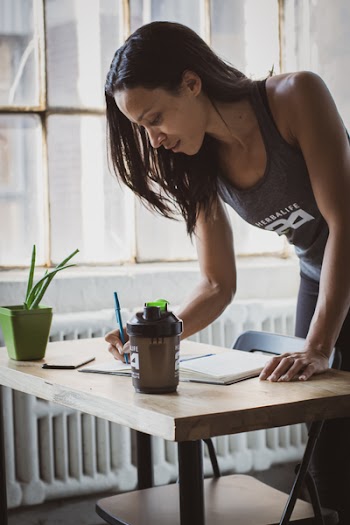 Woman Holding Pen While Writing on Book