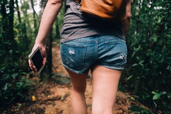 woman holding phone walking toward trees