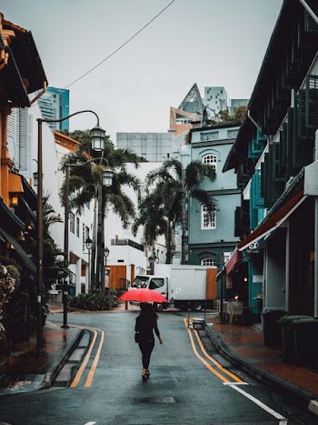 woman holding red umbrella walking on road between buildings at daytime