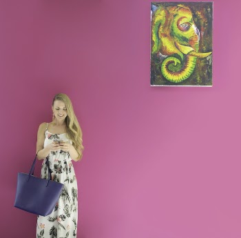 Woman Holding Smartphone and Blue Tote Bag While Leaning on Pink Wall With Elephant Painting
