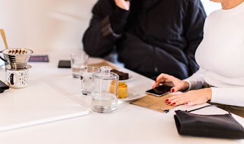 woman holding smartphone beside clear drinking glass on table