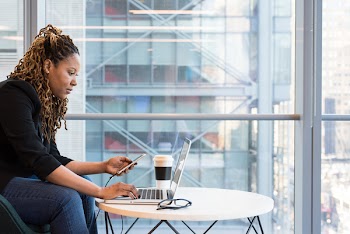 Woman Holding Smartphone Sitting in Front of Laptop on Table