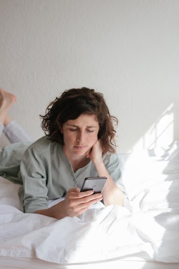 Woman Holding Smartphone While Lying In Bed
