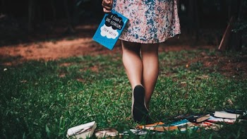 woman holding The Fault Against Our Stars book while walker on green grass