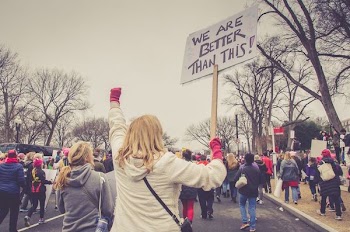 woman holding we are better than this placard