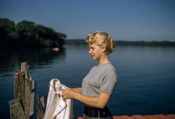 woman holding white textile standing beside body of water