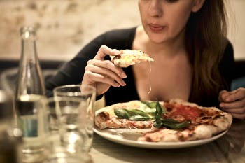 Woman Holds Sliced Pizza Seats by Table With Glass