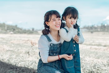 Woman Hugging Girl While Sitting on Grass Field