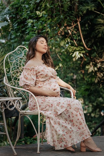 Woman in Beige and Red Floral Dress Sitting on White Armchair Outdoors