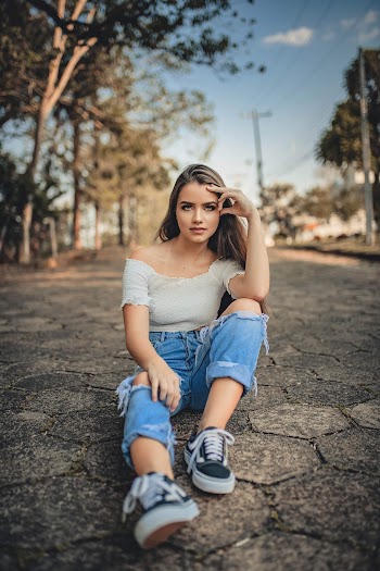 Woman in Beige Top and Blue Distressed Jeans Sitting on Floor Outdoors