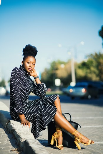 Woman in Black and White Polka-dot Dress Sitting Beside Pavement