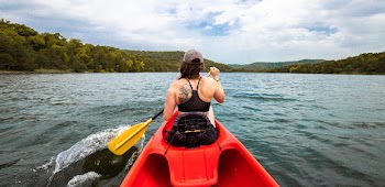 Woman in Black Bikini Top and Brown Hat Sitting on Red Kayak 