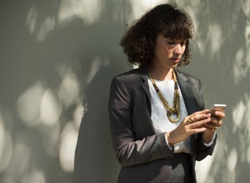 Woman In Black Blazer Holding A Smartphone While Standing Near Wall