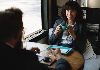 woman in black blazer sitting while holding blue teacup