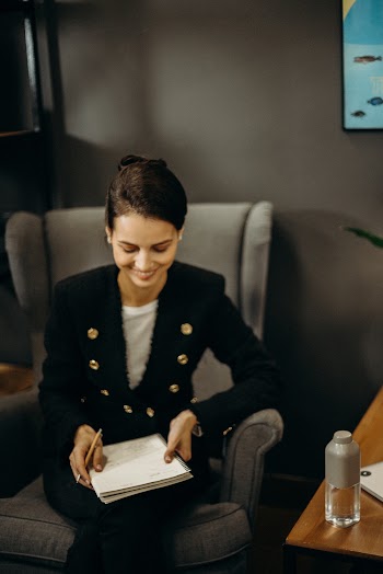 Woman in Black Coat Sitting on Sofa Holding a Notebook and  Pen