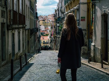 Woman in Black Coat Standing in Pathway Between Commercial Buildings