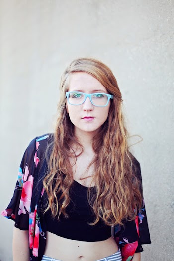 Woman in Black Crop Top Wearing Blue Sunglasses Taking Photography With White Background