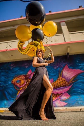Woman in Black Dress Holding Black and Yellow Balloons
